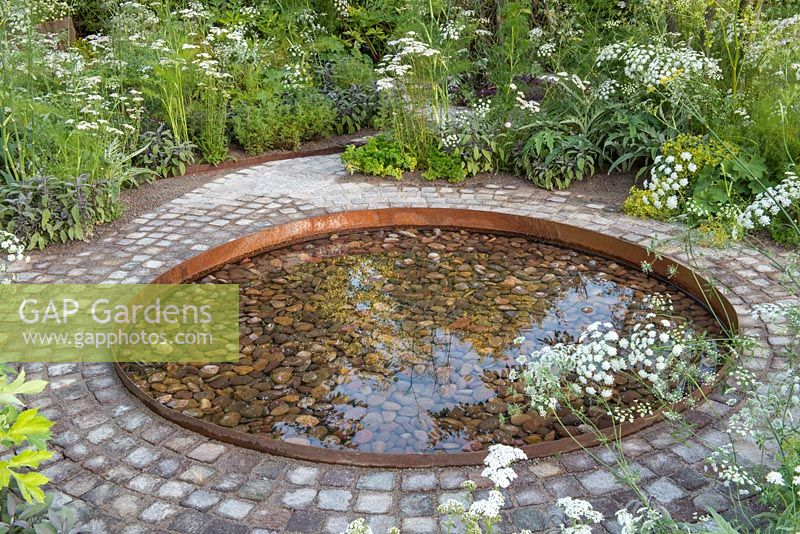 Circular pebble pool surrounded by a brick path, 'Health and Wellbeing Garden' RHS Hampton Flower Show, 2018. 
