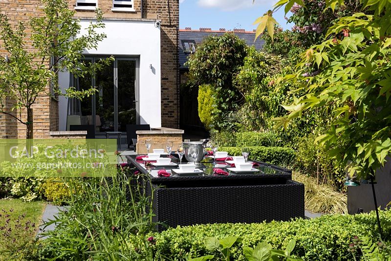 Black dining table and chairs on patio surrounded by flowerbeds in garden.