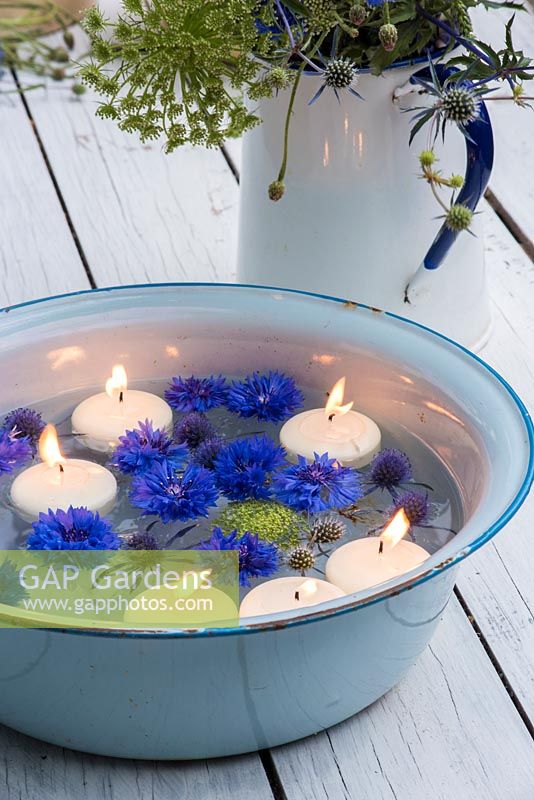 Floating cornflowers and candles in blue enamel bowl. 