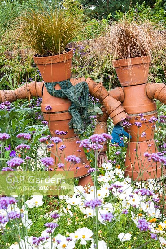 Flowerpot figures surrounded by flowers, annuals and perennials. 