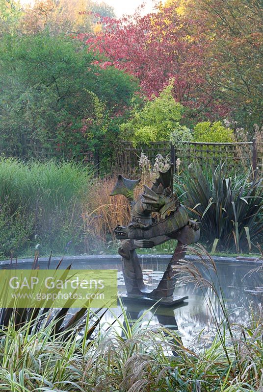 Miscanthus, Calamagrostis and Phormium with dragon sculplture. Knoll Gardens,  Dorset, UK