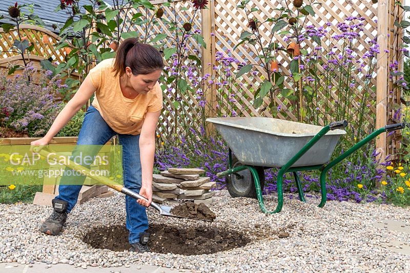 Woman digging circular hole for firepit with spade. 