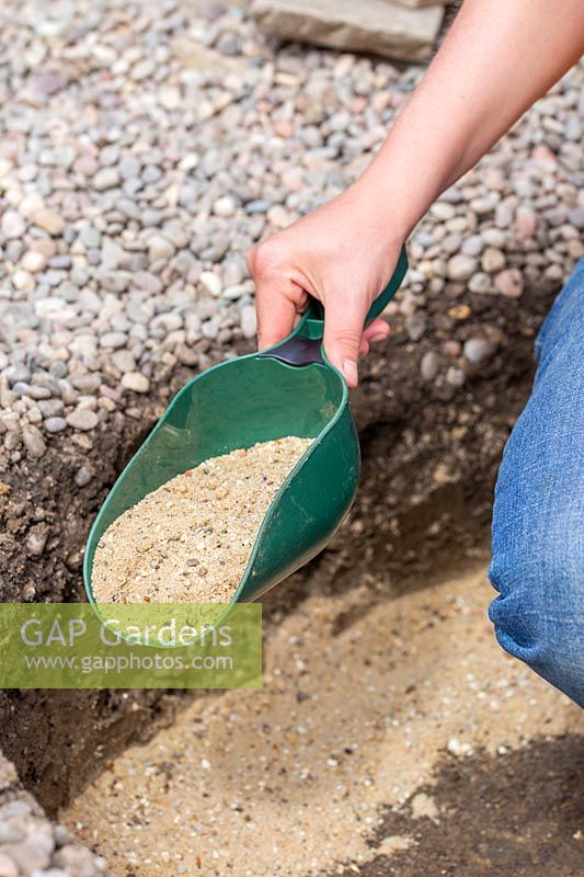Woman using plastic scoop to add gravel and sand in hole dug for firepit. 