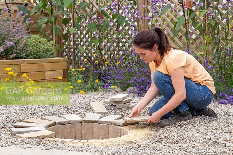 Woman placing pavers at edge of firepit. 