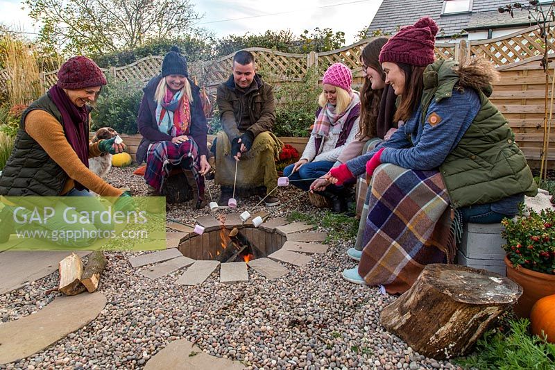 Group of people toasting marshmallows on fire in firepit. 