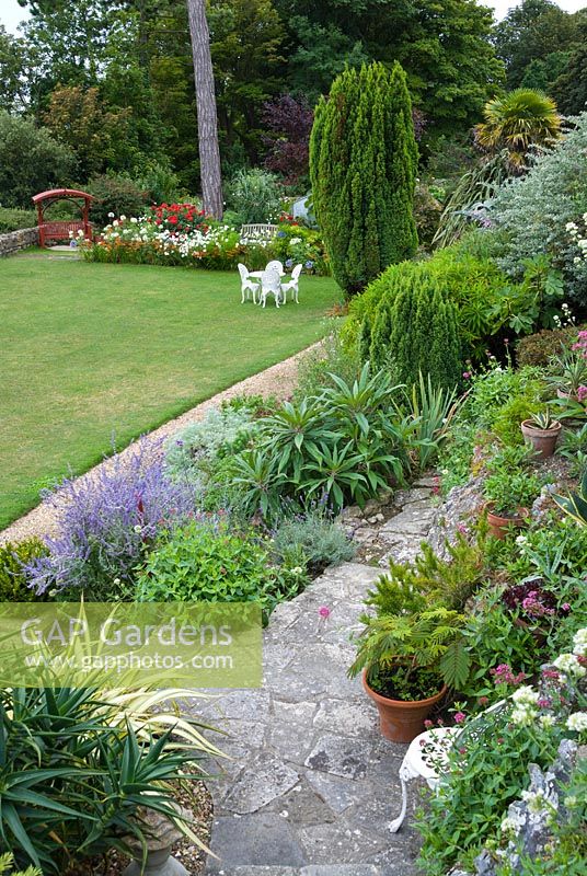 View of mixed planting, terrace and lawn in coastal garden, UK. 