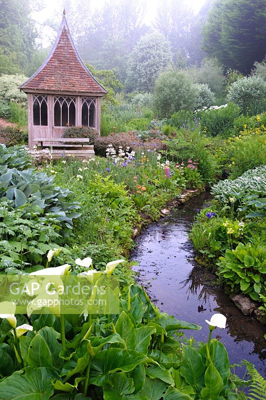 Summerhouse in the bog garden by a stream fringed with moisture loving plants. The Old Rectory, Netherbury, UK.