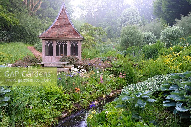 Summerhouse in the bog garden by a stream fringed with moisture loving plants. The Old Rectory, Netherbury, UK.
