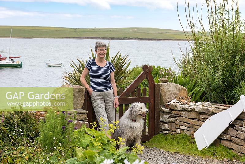 Sue Palmer in her seaside front garden overlooking Widewall Bay on South Ronaldsay, with Ollie the collie dog.