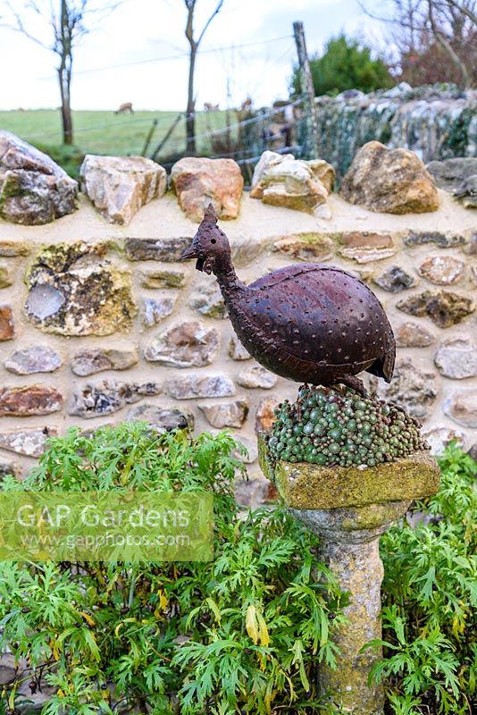 Decorative metal guinea fowl on a sempervivum encrusted stone plinth