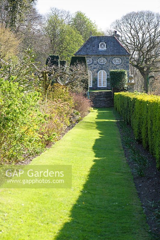 A grassy path between a box hedge and a mixed border leads towards the Orangery at Plas Brondanw, Penrhyndeudraeth, Gwynedd, Wales