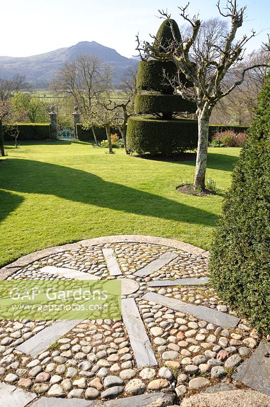 A decorative mosaic circle of slate and pebbles extends from the top path into the lawn. Plas Brondanw, Penrhyndeudraeth, Gwynedd, Wales