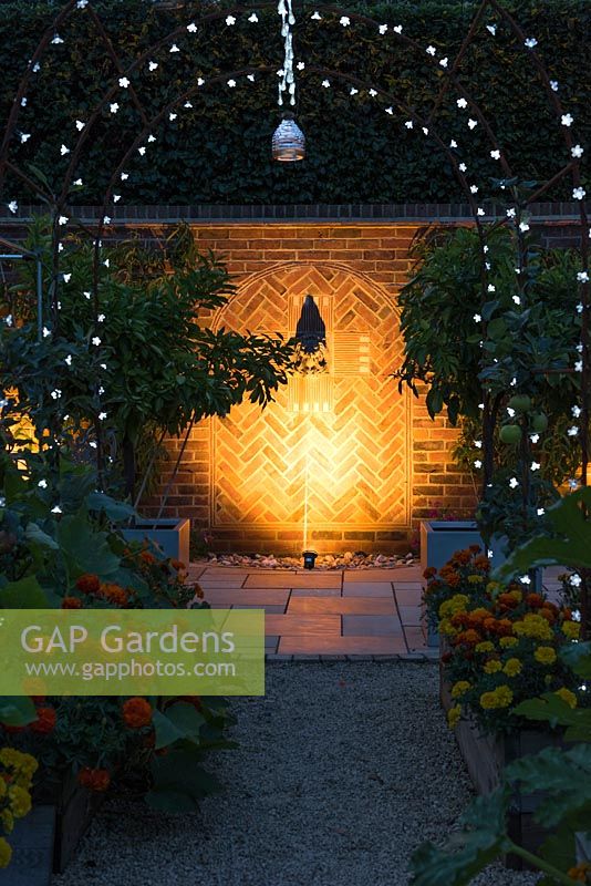 Pretty lighting hung on metal arches leading to an illuminated water feature.