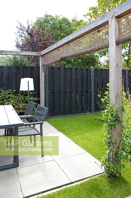 Garden patio and dining area surrounded by wooden pergola with wicker screens. 