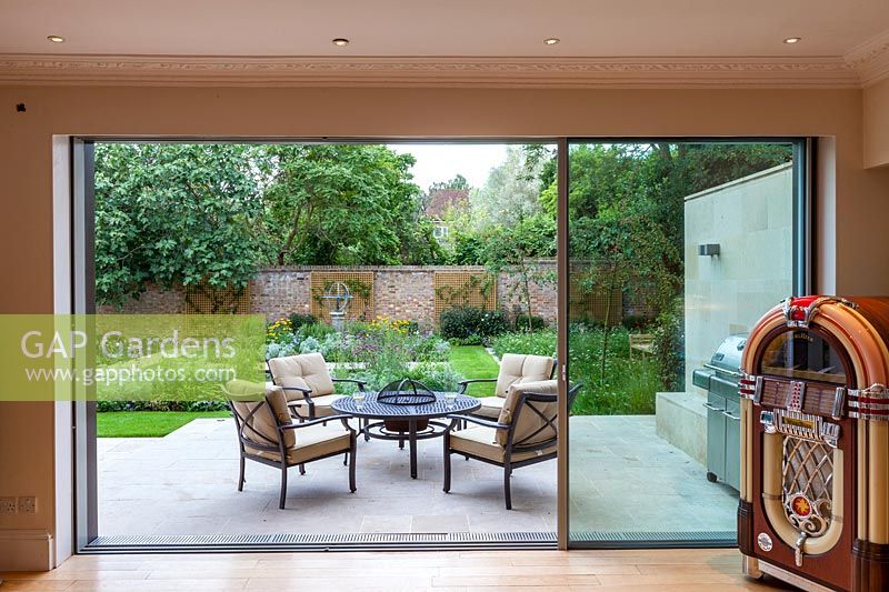 View from the inside out to terrace with table and chairs. Garden design by Peter Reader Landscapes.