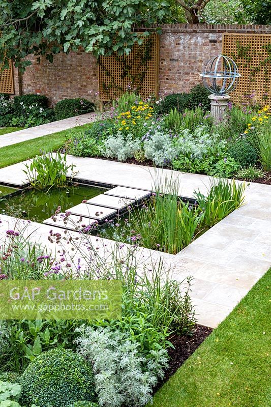View of formal pond with rill, surrounded by mixed beds with Armillary Sundial in walled city garden. Garden design by Peter Reader Landscapes.