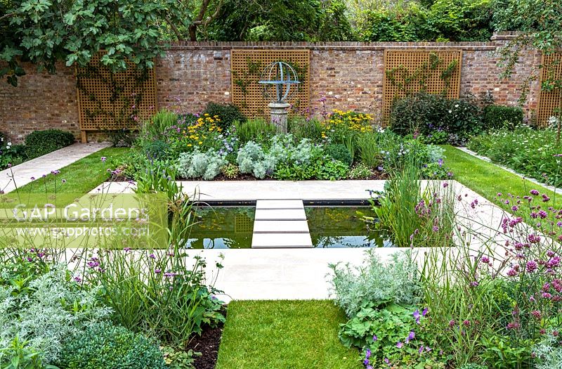 View of formal pond with rill, surrounded by mixed beds with Armillary Sundial in walled city garden. Garden design by Peter Reader Landscapes.