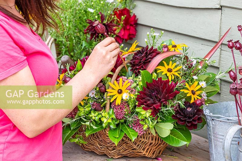 Woman inserting spray painted poppy seed head into a floral arrangement
