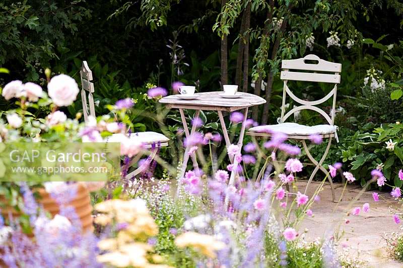 Seating area in cottage garden surrounded by soft, pastel summer flowers. Best of Both Worlds garden, Sponsored by BALI, RHS Hampton Court Palace Flower Show, 2018.
