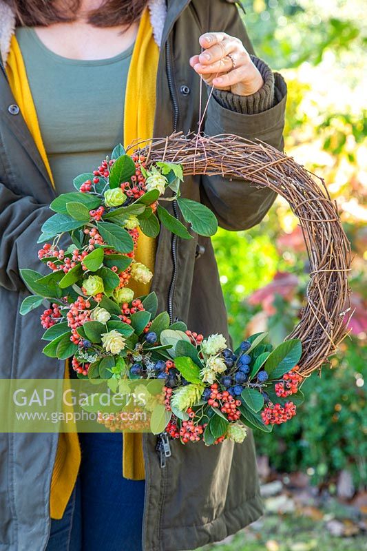 Holding autumnal deocrative wreath, with hop flowers, Cotoneaster and sloes.
