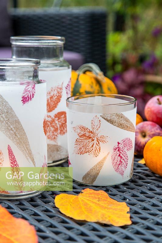 Trio of leaf-printed candle holders on table in greenhouse.