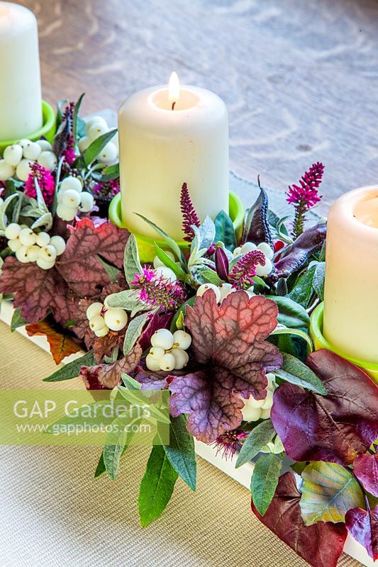 Autumn candle arrangement with Heuchera, Buddleja leaves, Hebe flowers, Lablab purpureus pods and Symphoricarpos - snowberry.