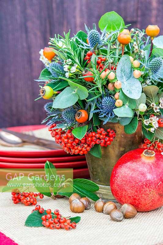 View of completed festive floral arrangement on table, with pomegranate, hazelnuts and crockery.