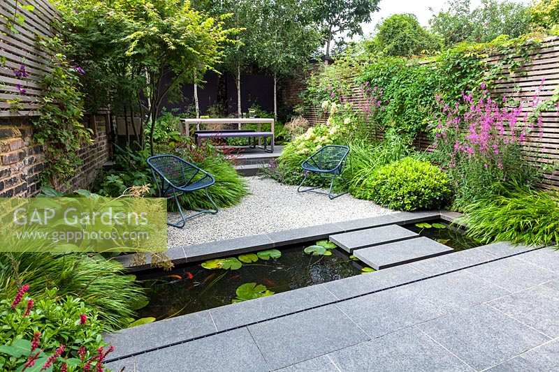 View of paved landing pad and narrow pool, across to gravelled area flanked by perennial planting. Garden design by John Davies Landscape.