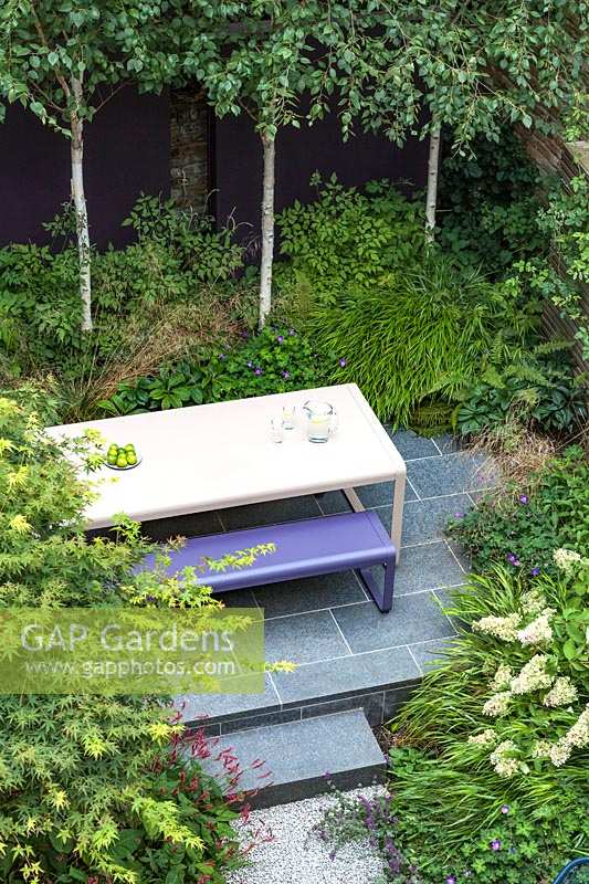 Overview of small urban garden, with raised terrace and table and bench. Garden design by John Davies Landscape.
