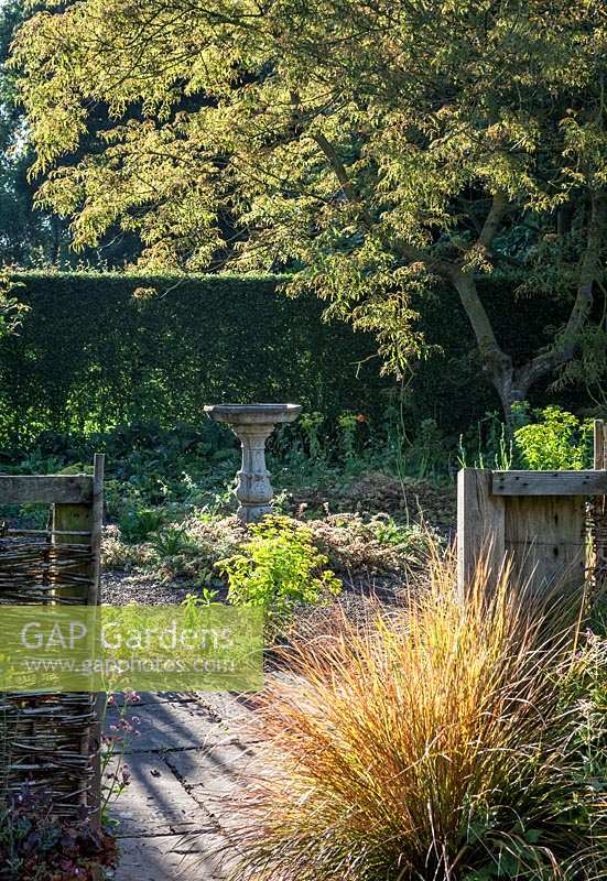 Stone birdbath and fence at Stillingfleet Lodge garden, Yorkshire, UK