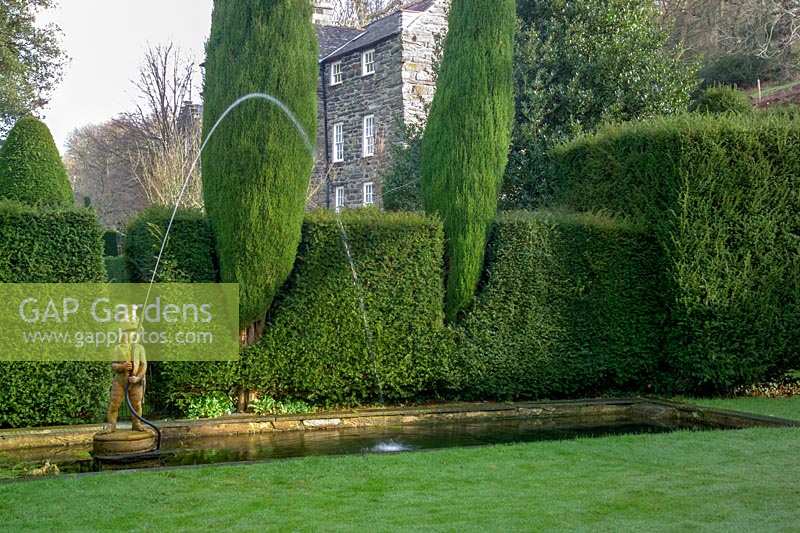 'Fireman' fountain in a pond featuring evegreen shaped Yew hedging in the bakground, 
Plas Brondanw, North Wales, UK  

