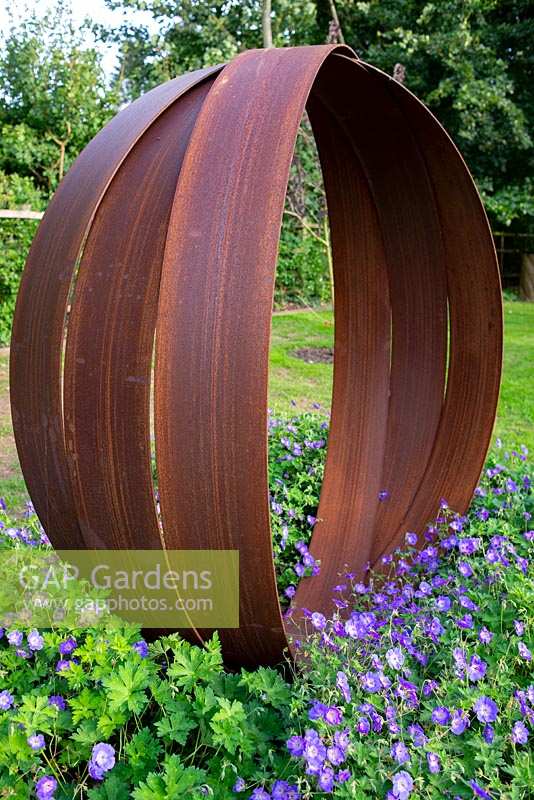 Rusted steel sculpture inspired by a Russian wedding ring designed and made by Dominic Watts. Underplanted with Geranium Rozanne 'Gerwat'. 