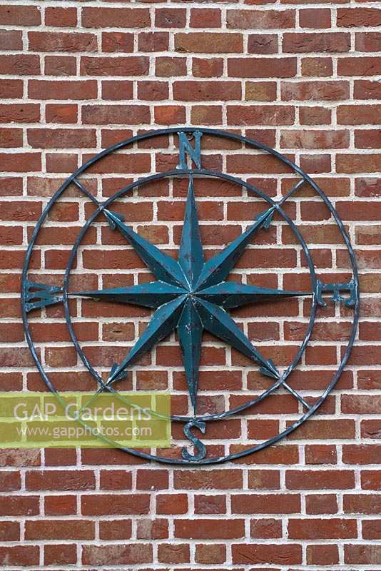 Large metal compass on side of brick wall. 