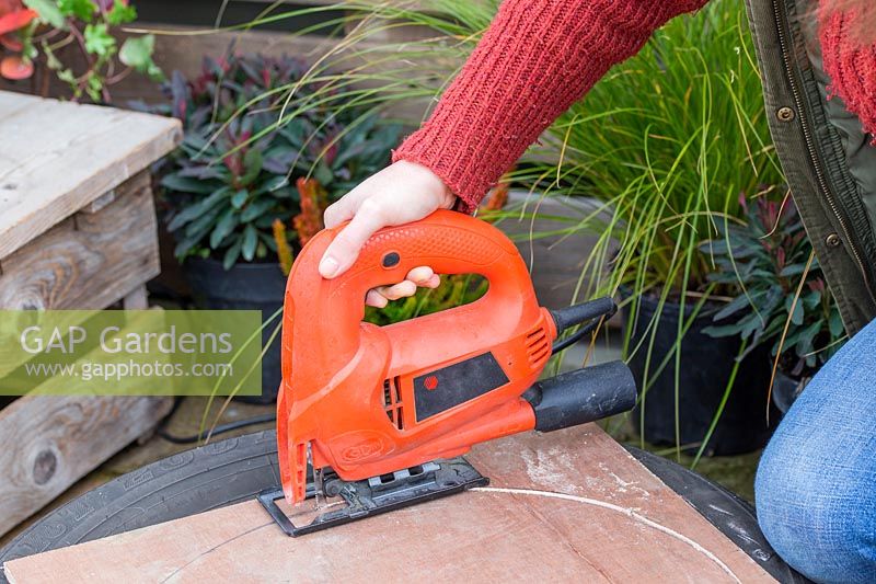 Woman using jigsaw to cut circle of hardboard for base of planter.