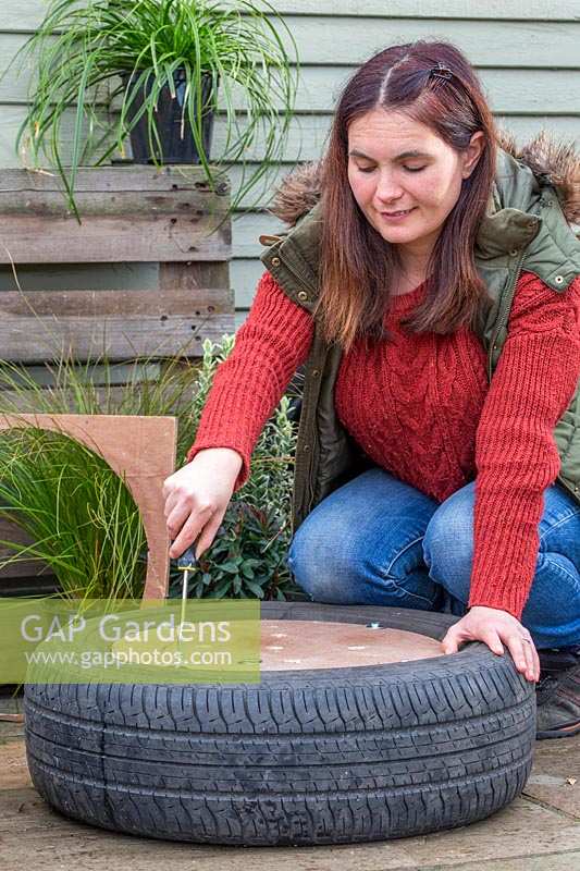 Woman using washers and bolts to secure wooden base onto tyre planter.