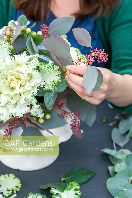Woman adding seeded Eucalyptus to arrangement with ornamental cabbage.
