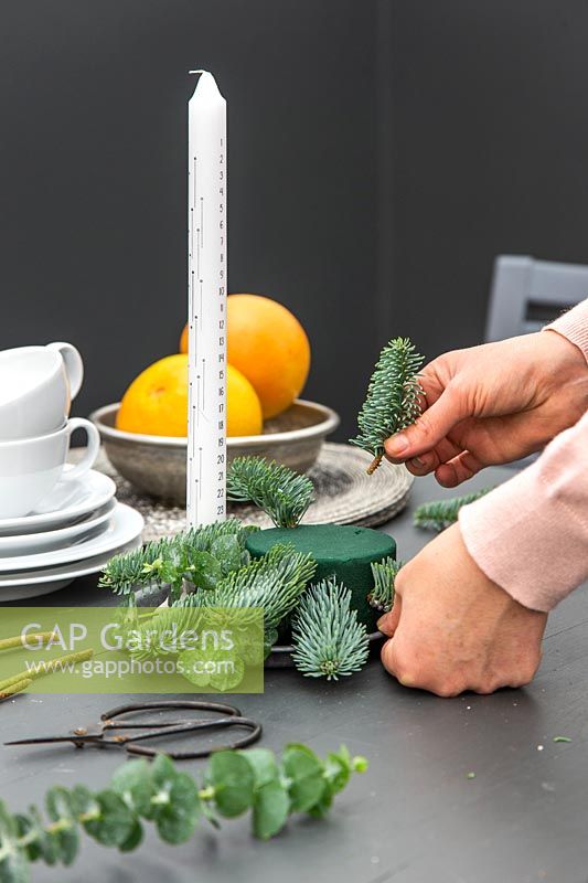 Woman making Christmas advent candle arrangement at breakfast table.