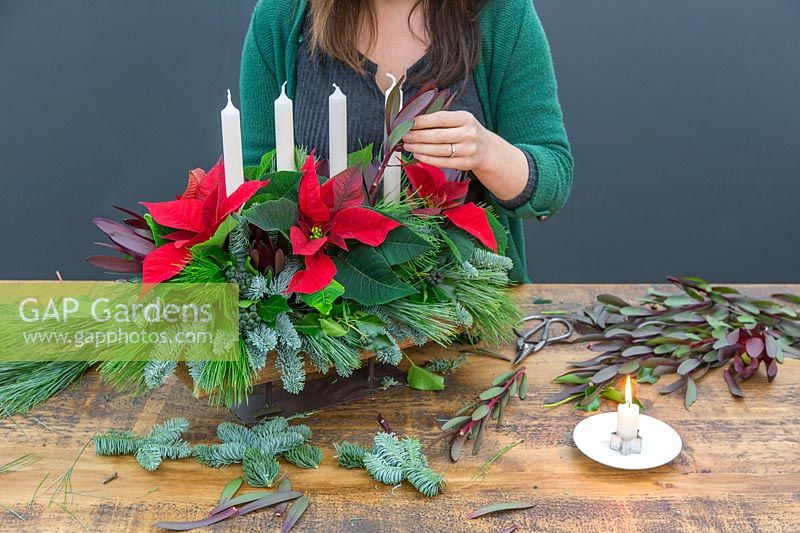Woman inserting Leucadendron stem into christmas candle arrangement.