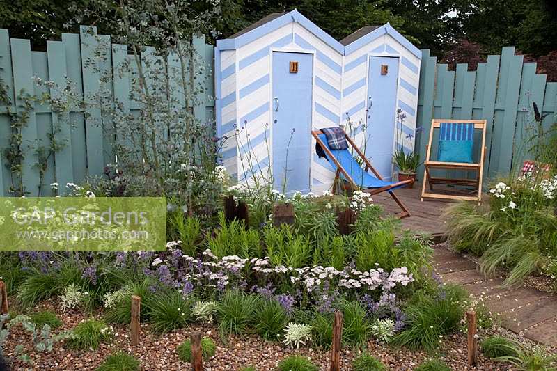 Blue and white beach huts and deck chairs bordered by blue and white coastal planting. Southend Council 'By The Sea' garden at RHS Hampton Court Flower Show, London, 2017.
