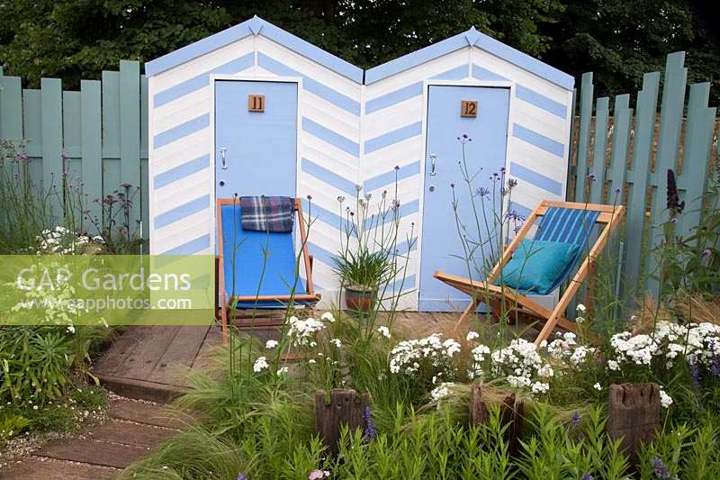 Blue and white beach huts and deck chairs bordered by blue and white coastal planting. Southend Council 'By The Sea' garden at RHS Hampton Court Flower Show, London, 2017.