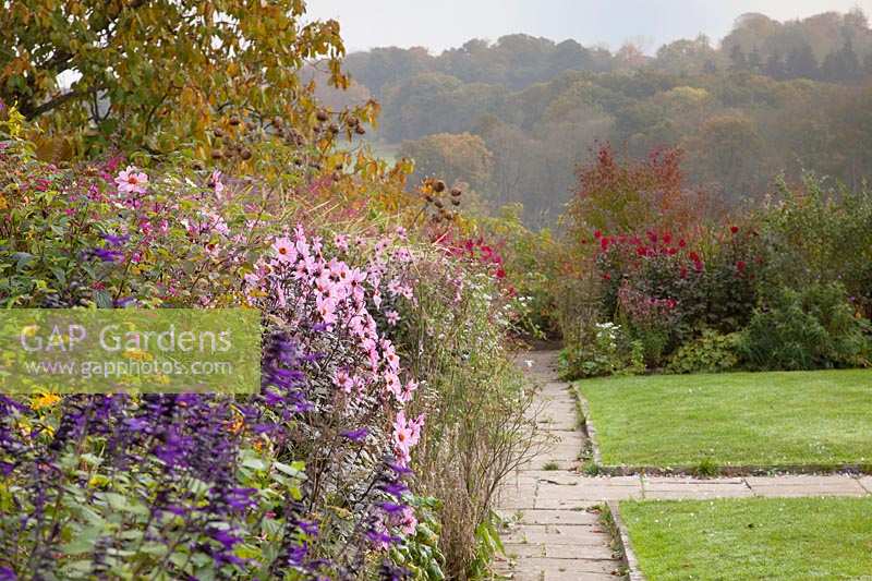 Colourful autumn border alongside stone path and lawn. Gravetye Manor, Sussex, UK. 