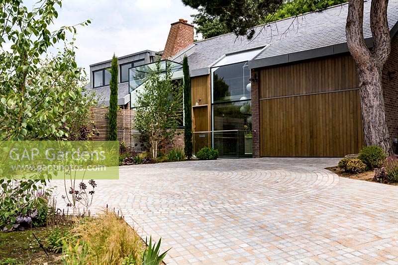 Contemporary house with circular stone sett driveway with edged with planted beds

