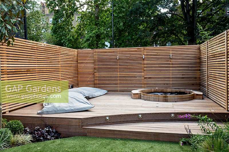Contemporary garden surrounded by a cedar battened trellis screen for privacy around a stepped decking area with 

hot tub and large garden lounge cushions
