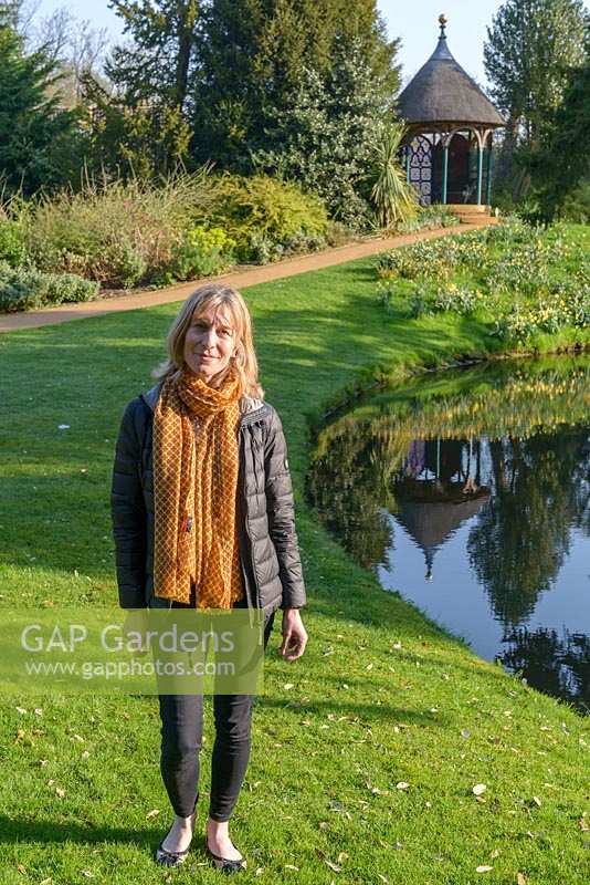 Woman with jacket and scarf standing on lawn by water
