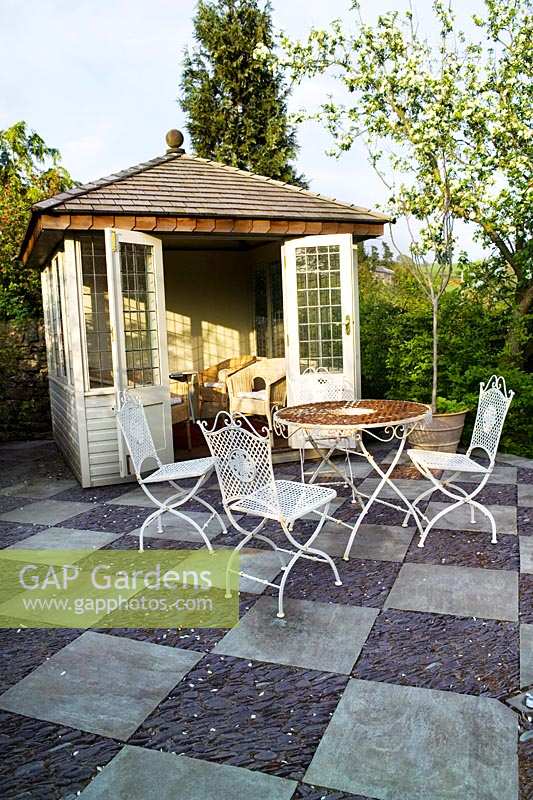 View of summerhouse with paved patio and garden table and chairs. Summerdale Garden, Cumbria, UK. 
