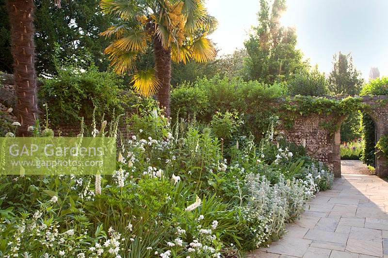 White themed Fitzalan Chapel Garden with archway through stone wall and palm trees. Arundel Castle, West Sussex, UK