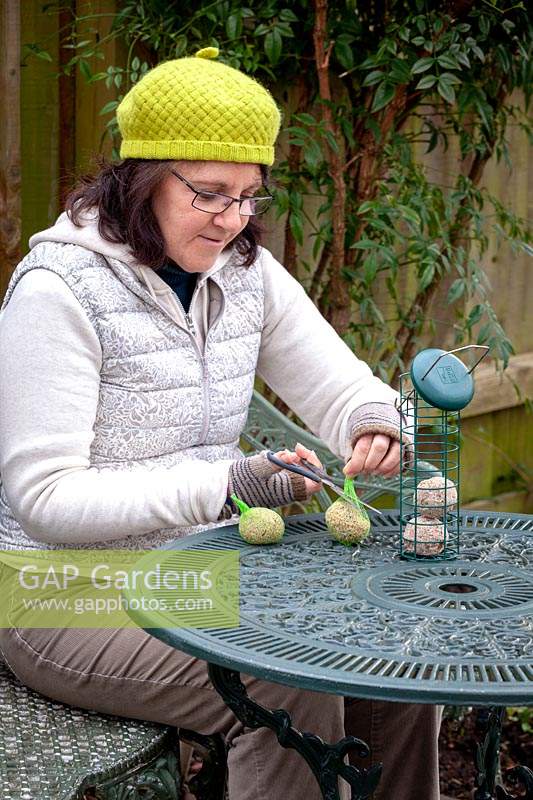 Woman taking netting off fat balls and filling a bird feeder.