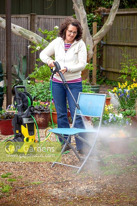 Woman cleaning garden furniture with a pressure washer. 