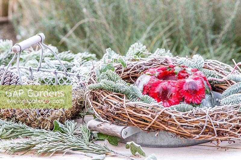 View of frozen floral arrangement displayed outside with frosted pine, cones, ivy and woven wreath.  