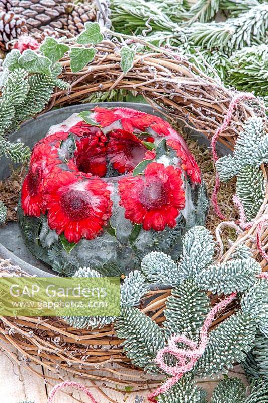 View of frozen floral arrangement displayed outside with frosted pine, cones, ivy and woven wreath.  